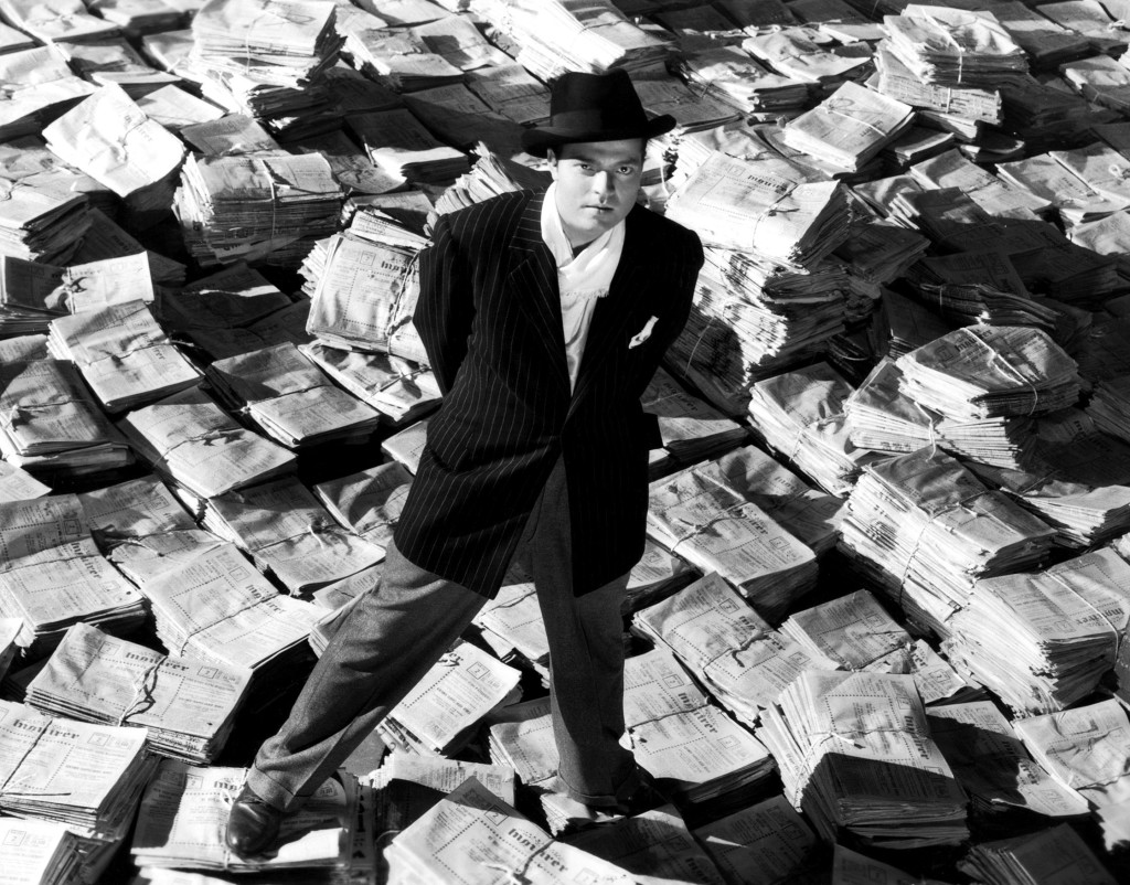 CITIZEN KANE, Orson Welles, 1941, astride stacks of newspaper
